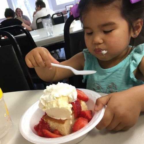 A child eats a huge bowl of strawberry shortcake with whipped cream